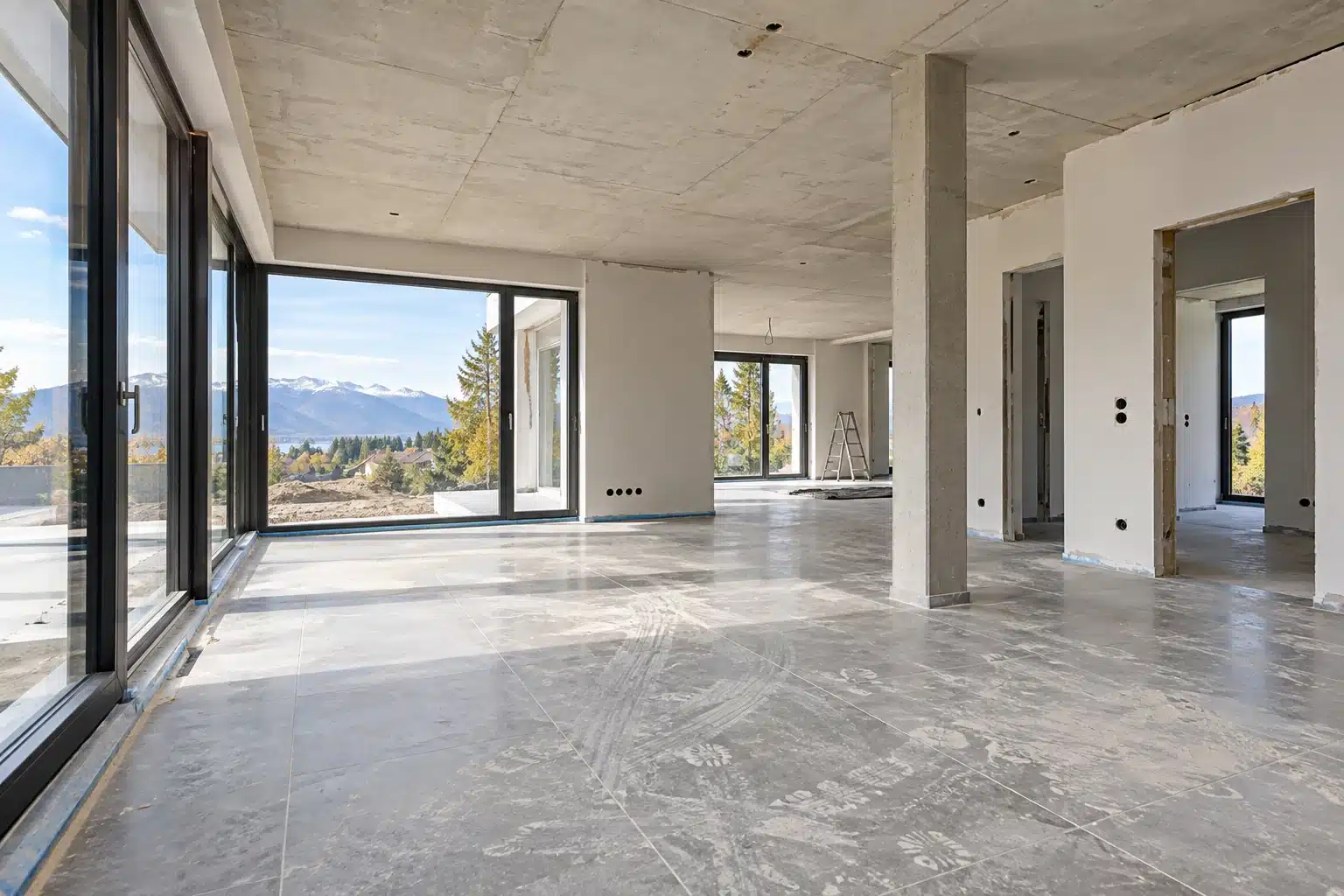Moderner Rohbau mit großen Glasflächen, Betondecke und staubigen Böden vor der Baureinigung