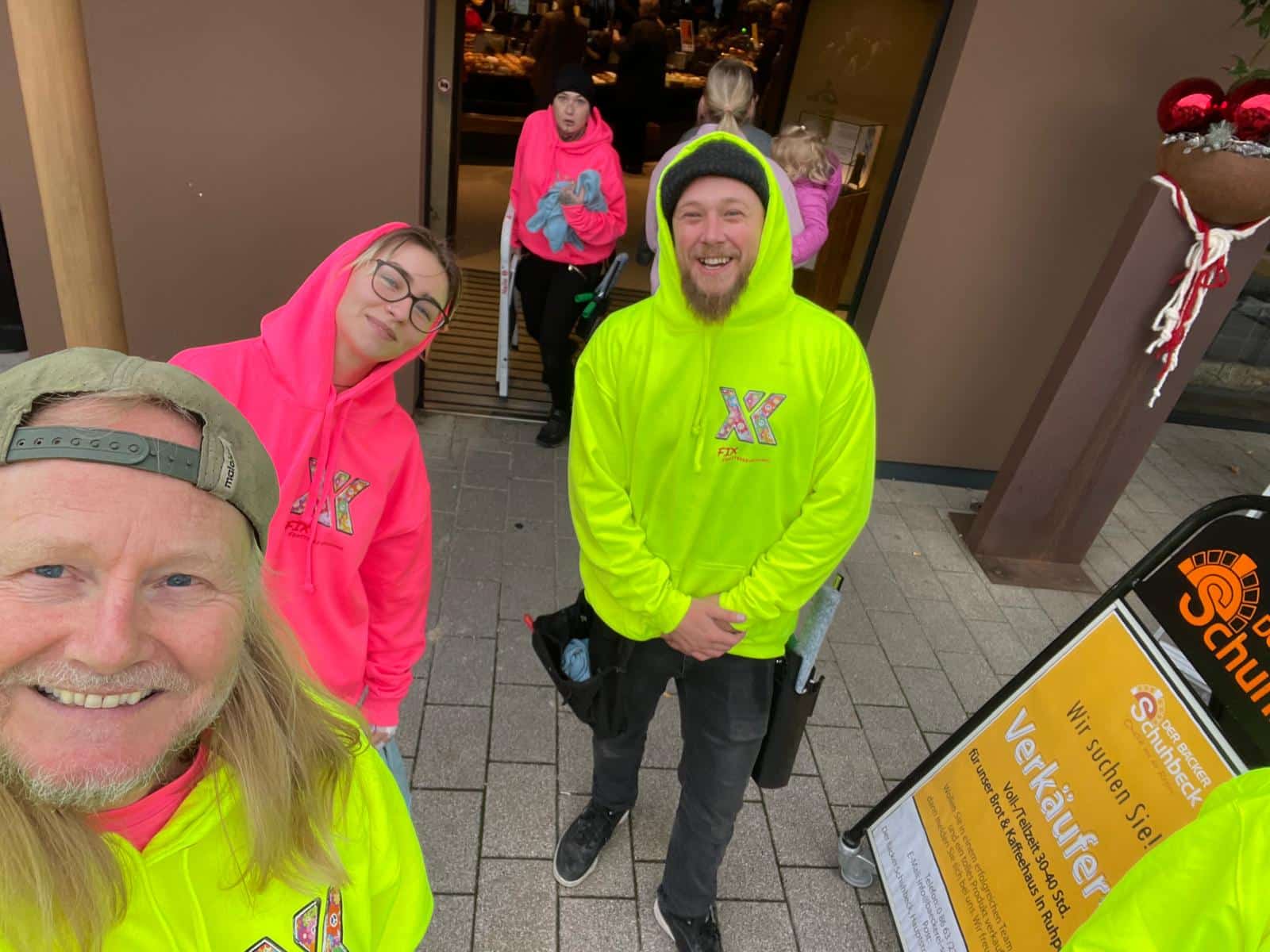 Das FIX-Team in pinker und neongelber Arbeitskleidung vor einem Geschäft