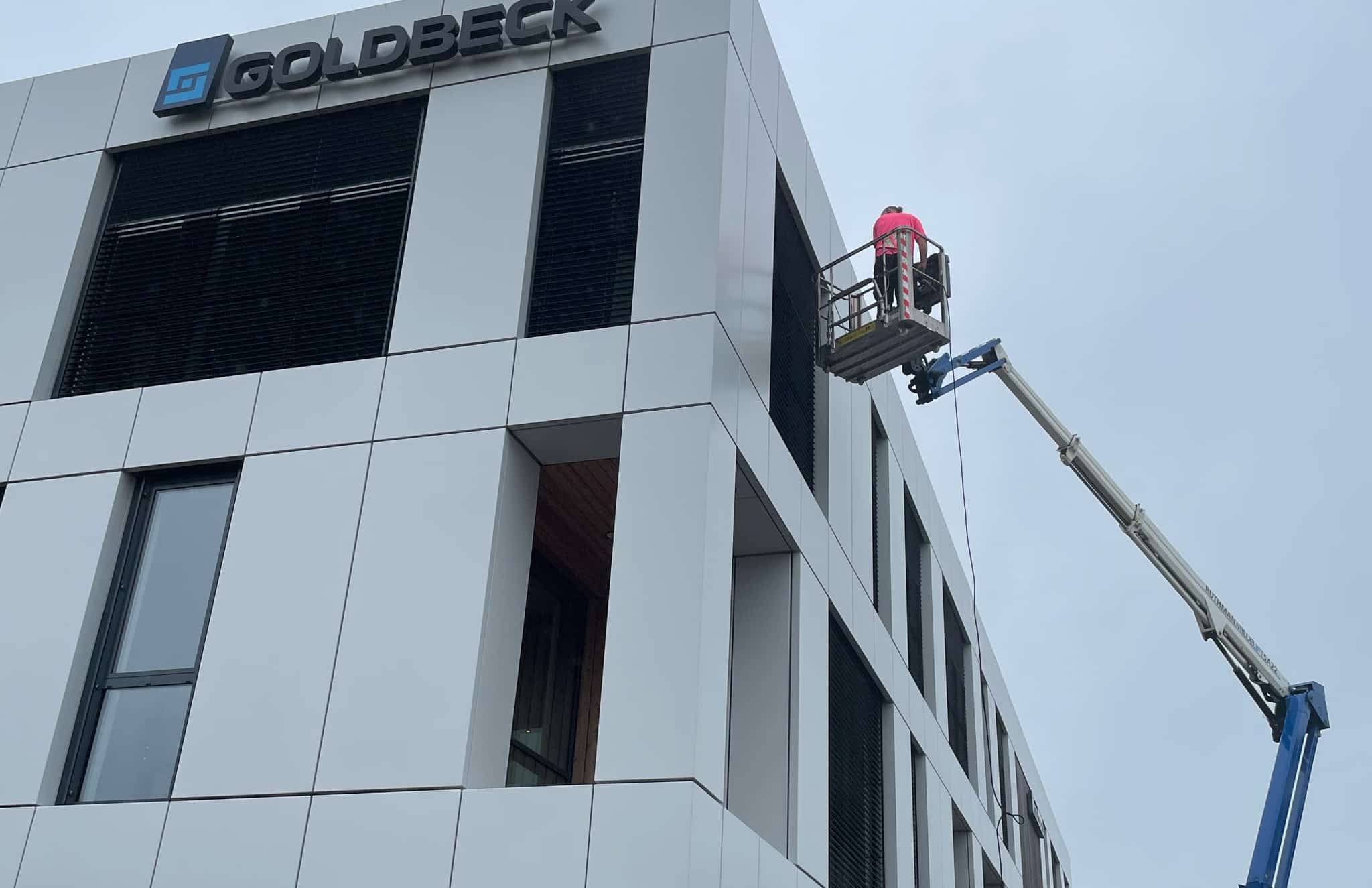 Mitarbeiter auf einer Hubarbeitsbühne bei der Lamellenreinigung am GOLDBECK-Gebäude in Rosenheim